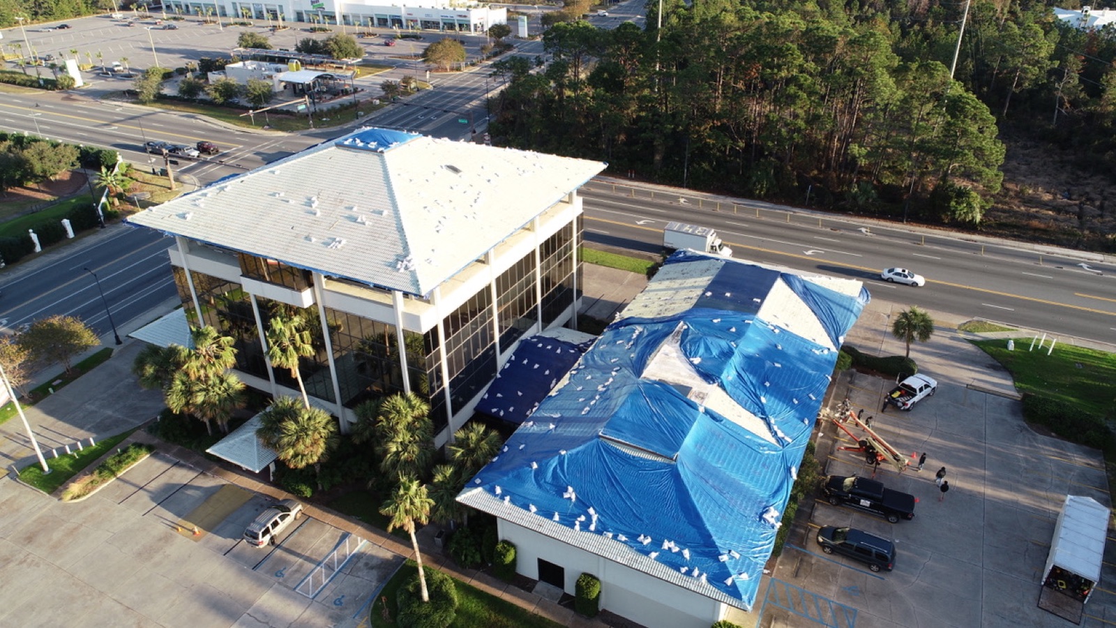 Commercial buildings covered in torn failing blue tarps after storm damage